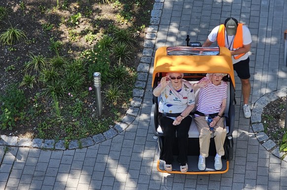 Auf dem Bild sitzen zwei Damen in der Rikscha und der Fahrer steigt auf.