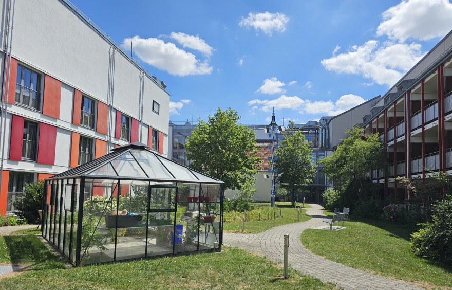Auf dem Bild ist der Garten des Theresianums mit Gewächshaus,Teich und Maibaum zu sehen.