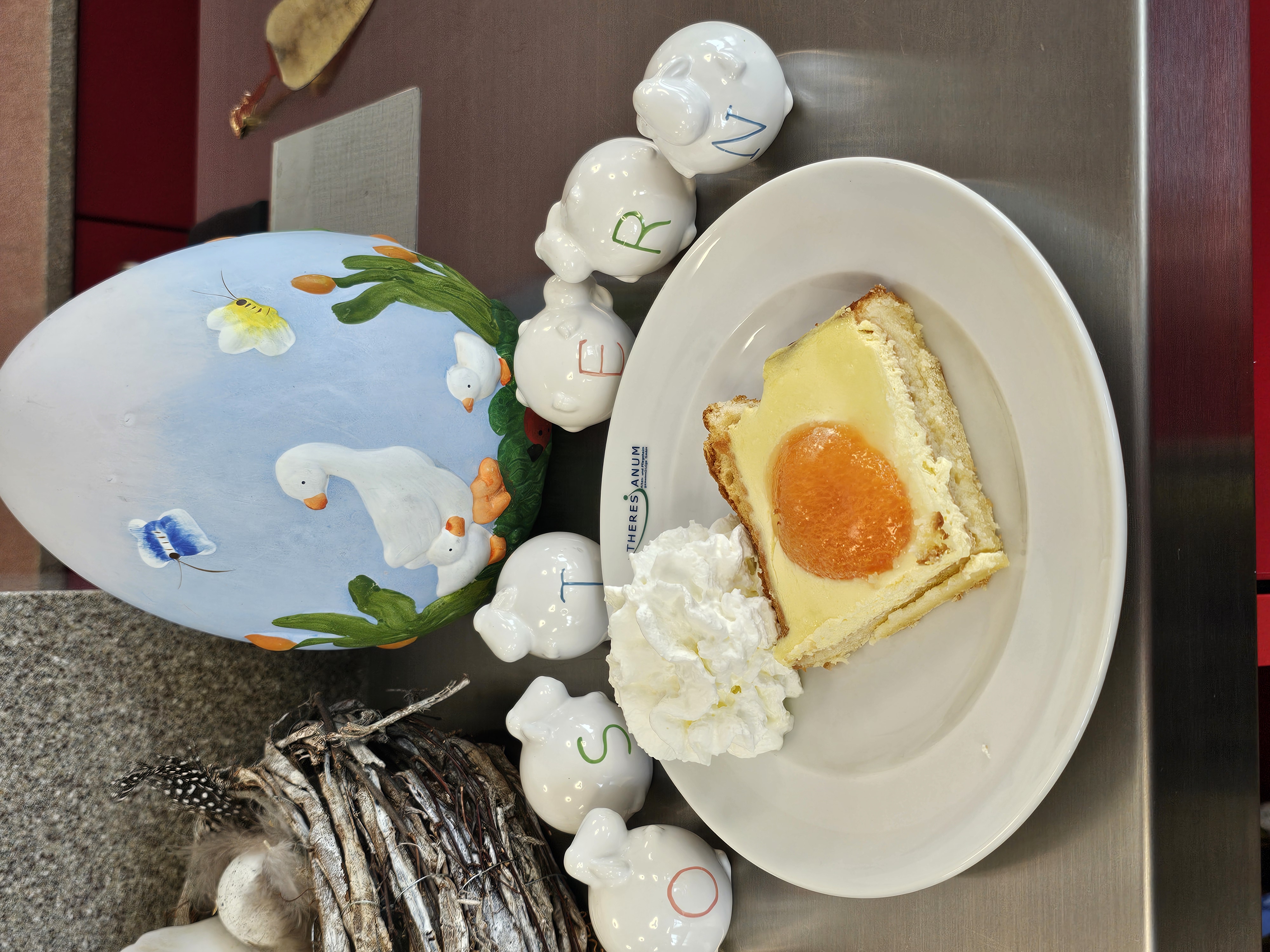 Auf dem BIld sieht man selbstgebackenen Spiegeleierkuchen, sowie ein Osterei und Porzellanschafe mit Buchstaben,welche das Wort Ostern ergeben.