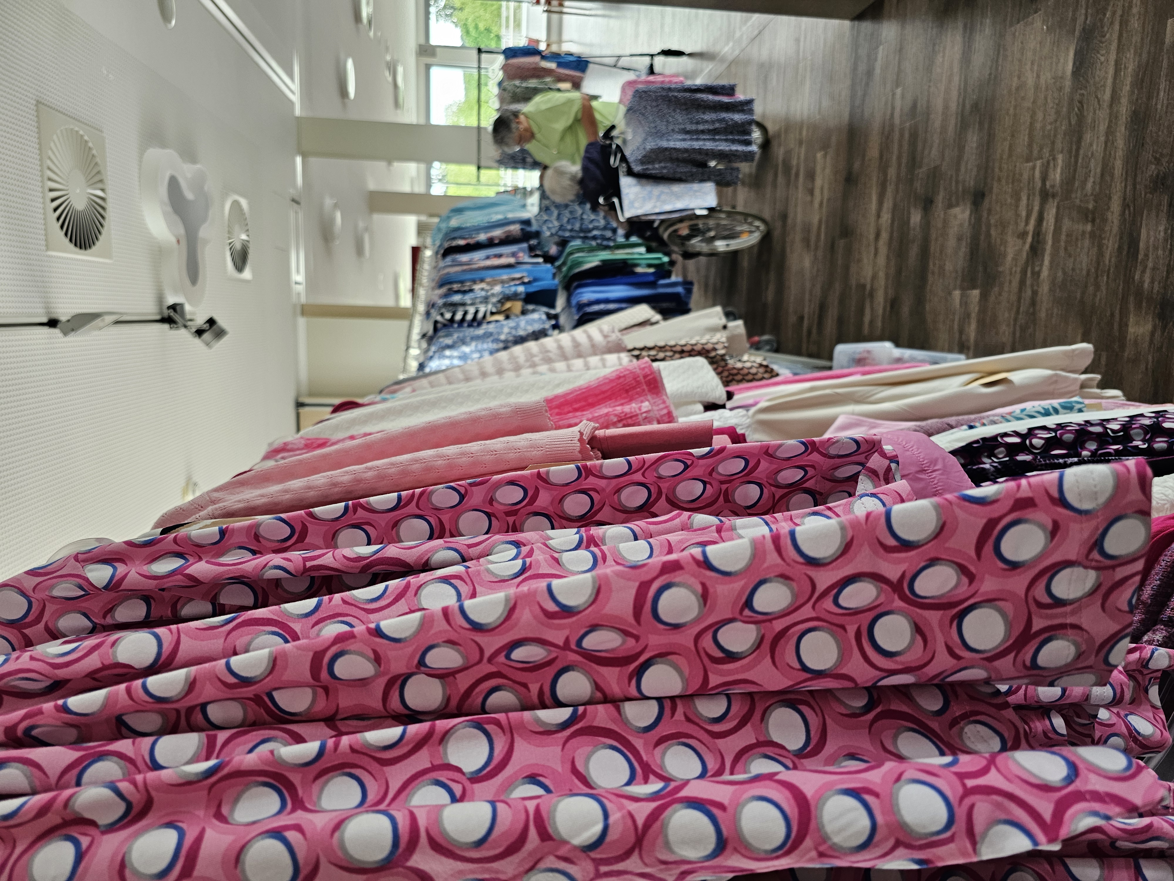 Auf dem Bild sind verschiedene Kleidungsstücke in verschiedenen Farben auf Ständern zu sehen. Sie hängen in der Reihe.